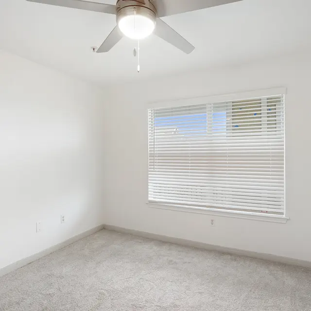 A room with a ceiling fan and a window with blinds.